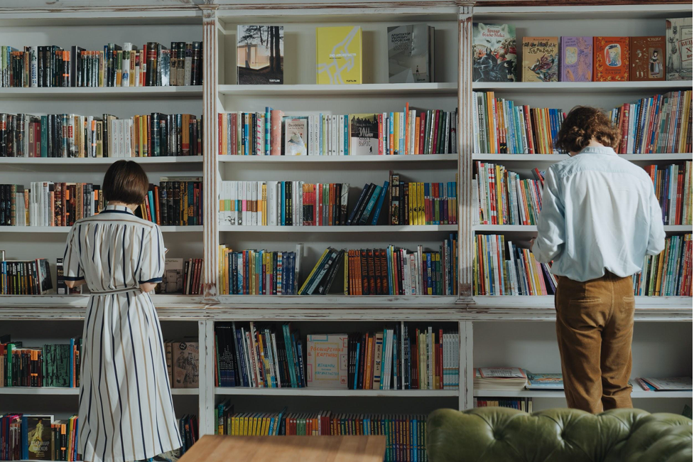 A man and a woman reading books, infront of a book shelf
